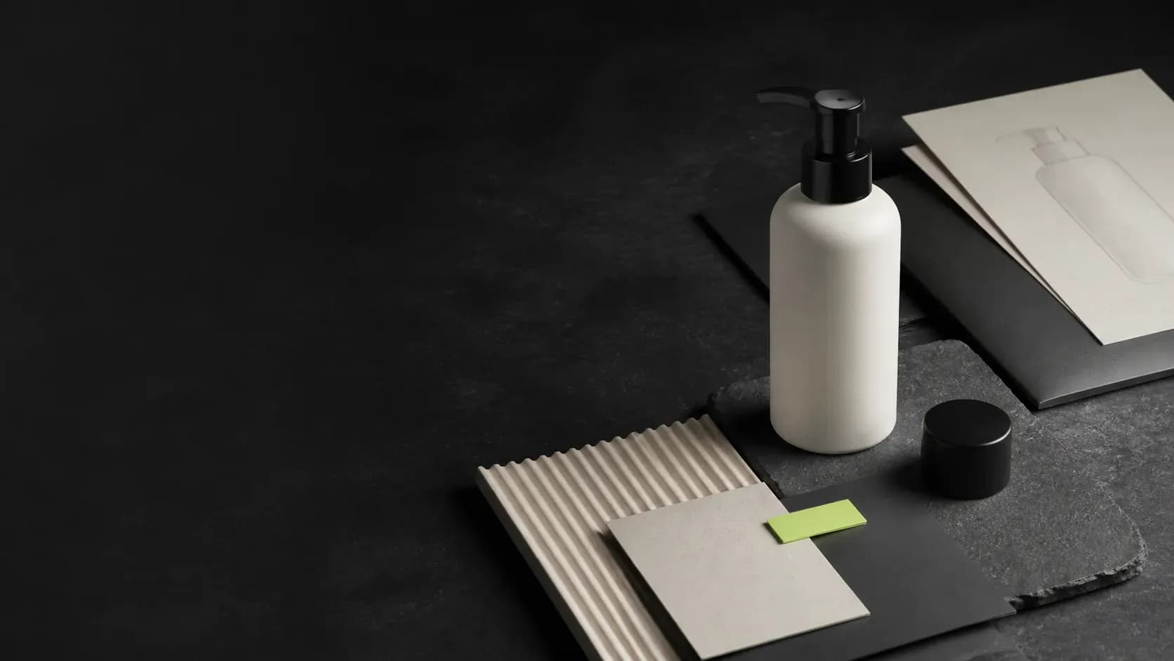 An unbranded haircare container, packaging material samples, and blank project sheets arranged on a dark planning workspace.
